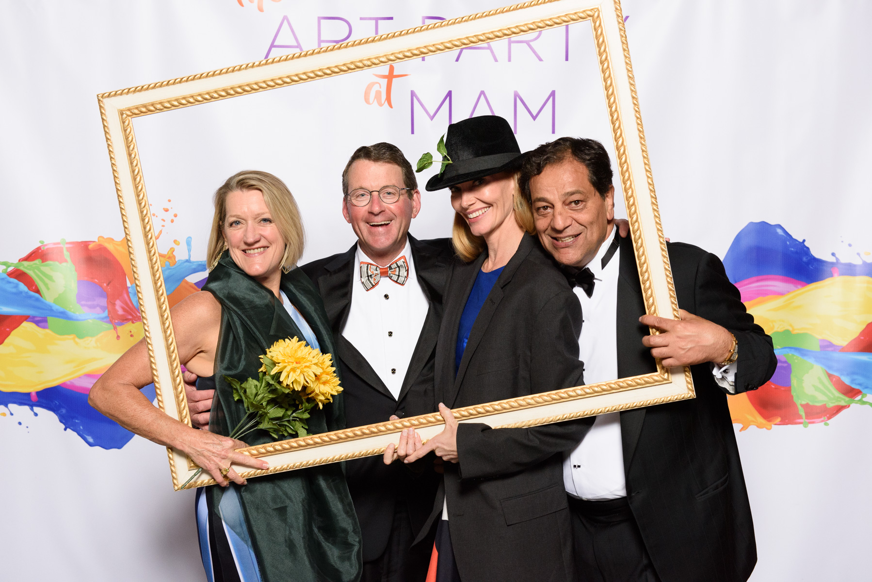 Four Patrons attending the Art Party pose in front of a banner with an empty picture frame