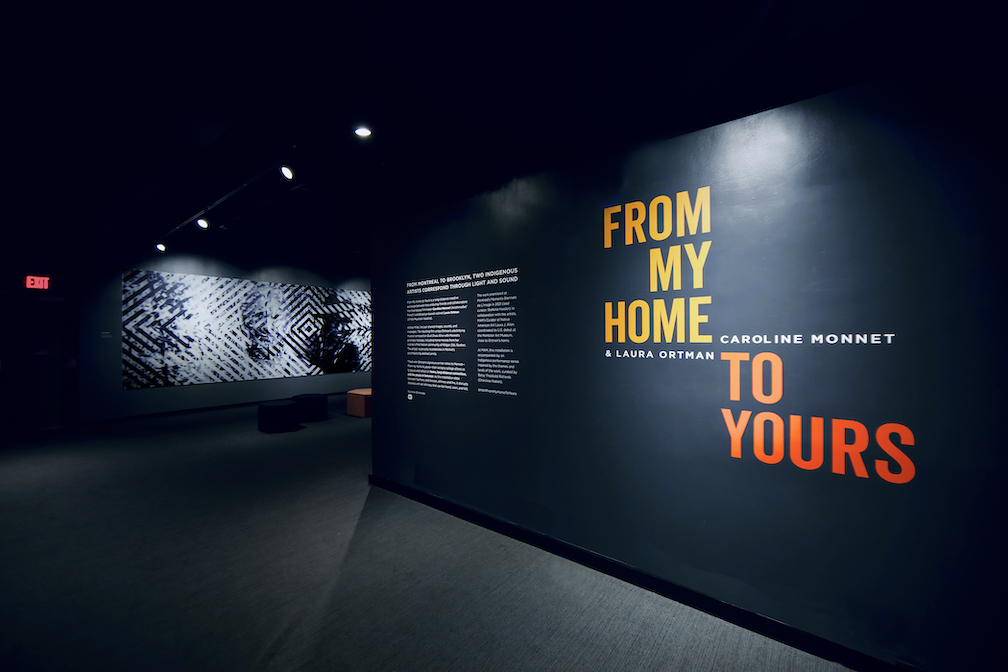 The entrance to the gallery where the film "From My Home to Yours" is projected in the background. 