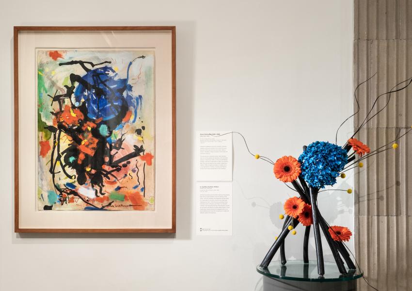 A floral arrangement sits in front and to the right of an abstract painting in MAM's galleries. This is part of Art in Bloom, a biennial floral design exhibition.