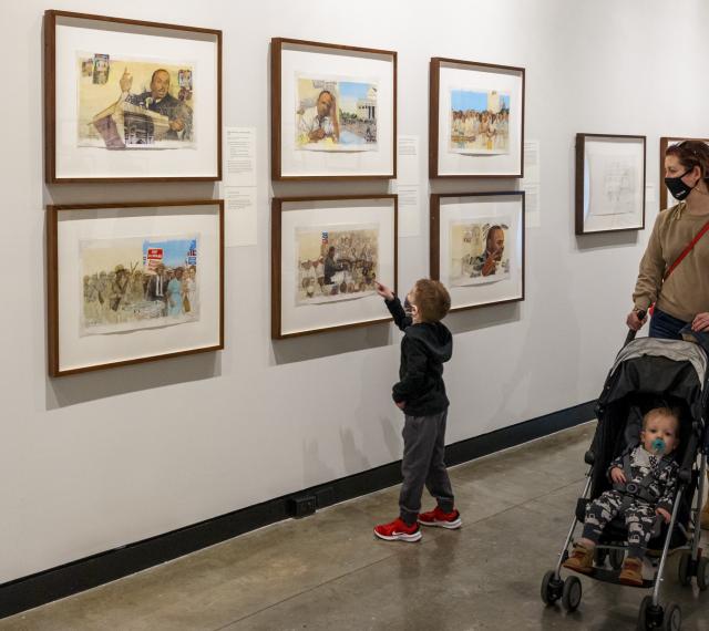 A family walking through the gallery with a small child pointing at paintings on the wall.