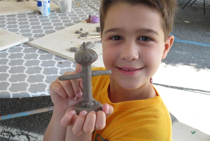 Camper holding up their clay figure that they created in SummerART Camp (Ceramics Hand-building) 