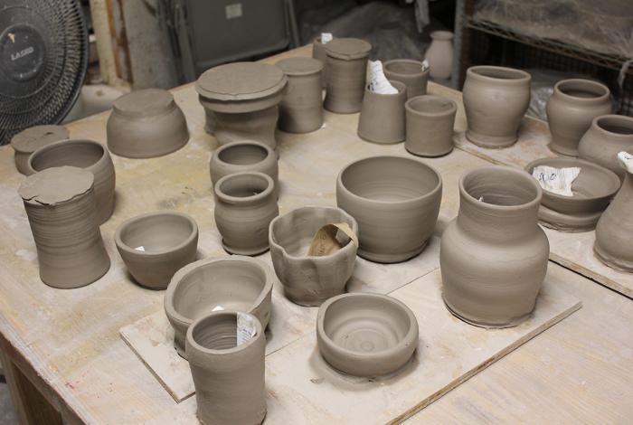 Multiple clay vessels (vases, bowls, cups) sitting on a table in a ceramics studio