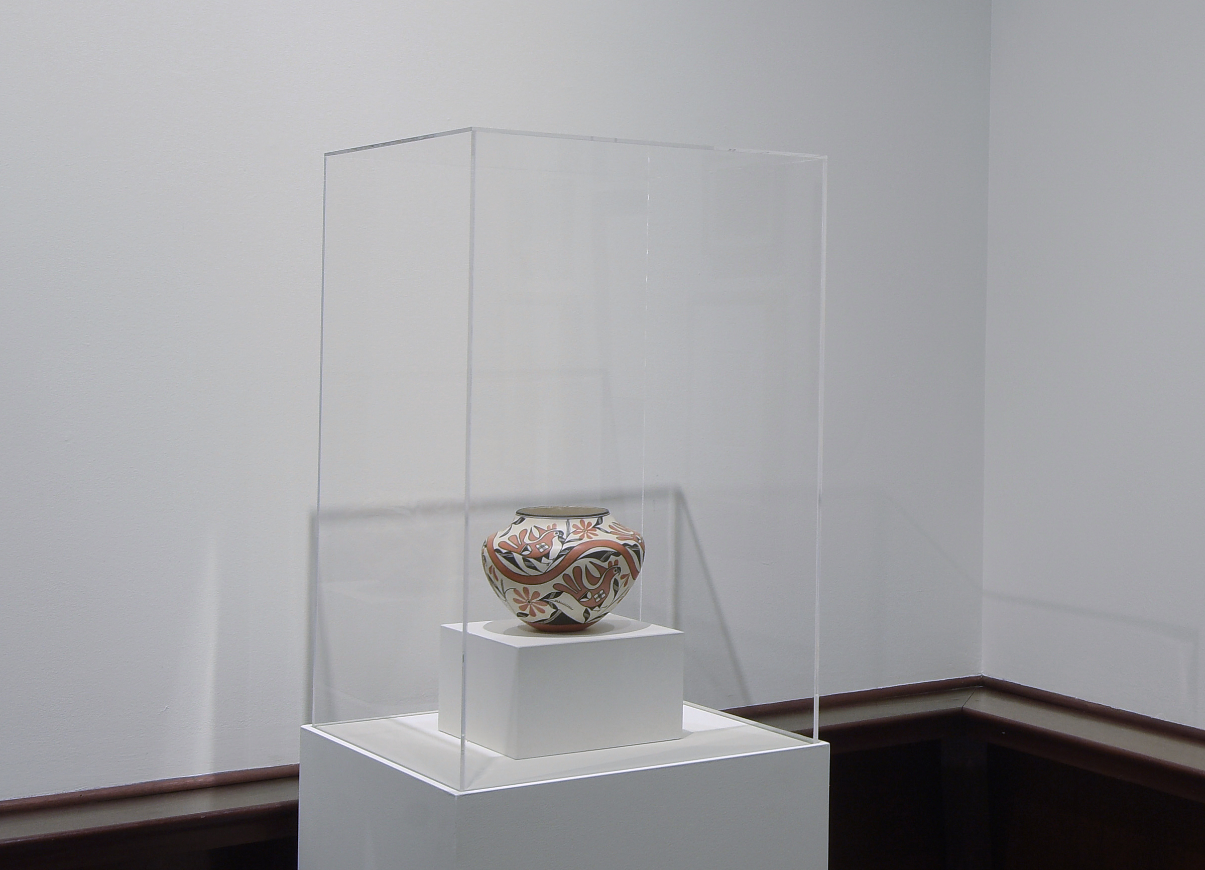 A traditional handmade and painted pot is sitting in a glass case in a MAM gallery.