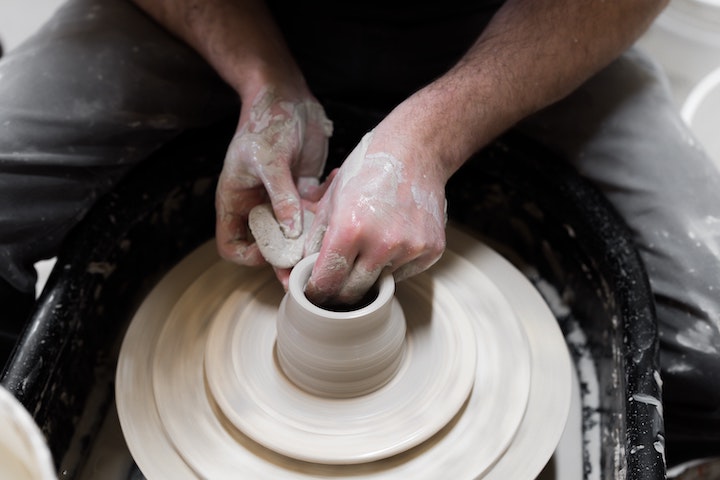 Adult hands working on clay on the pottery wheel.
