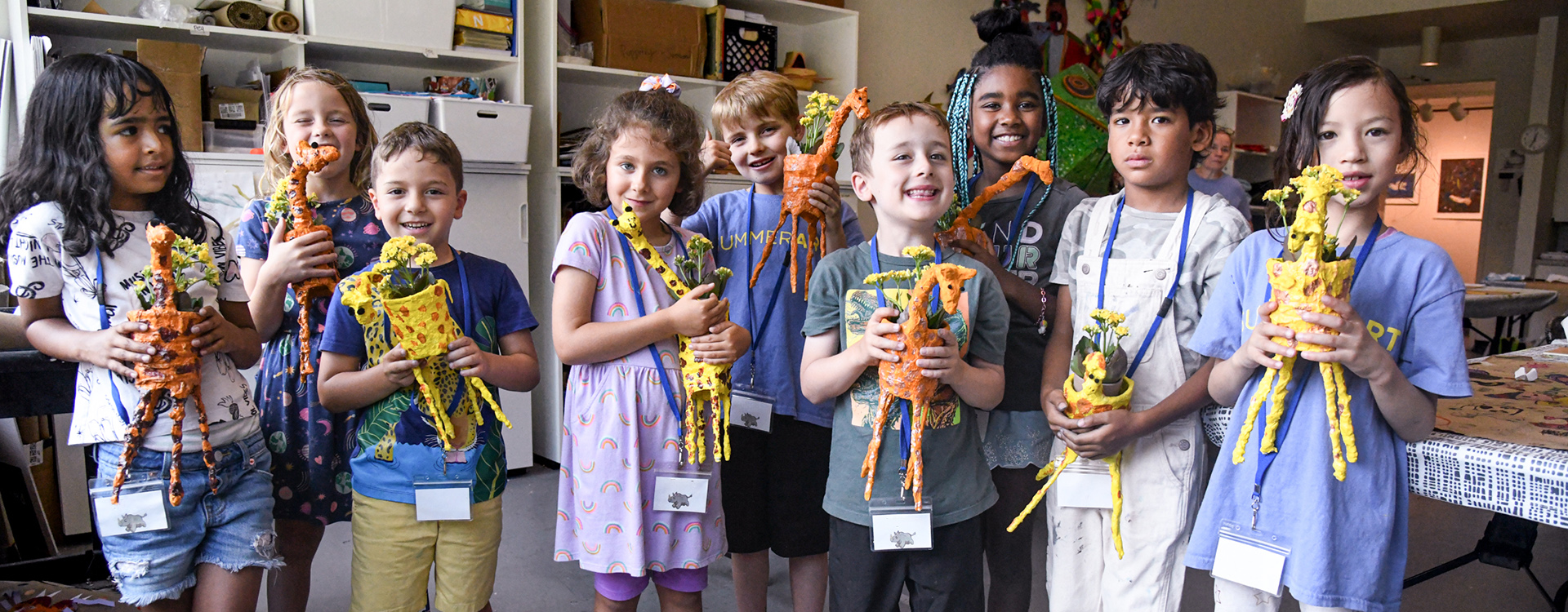 Group of SummerART campers holding up giraffe shaped flower pots and smiling for the camera