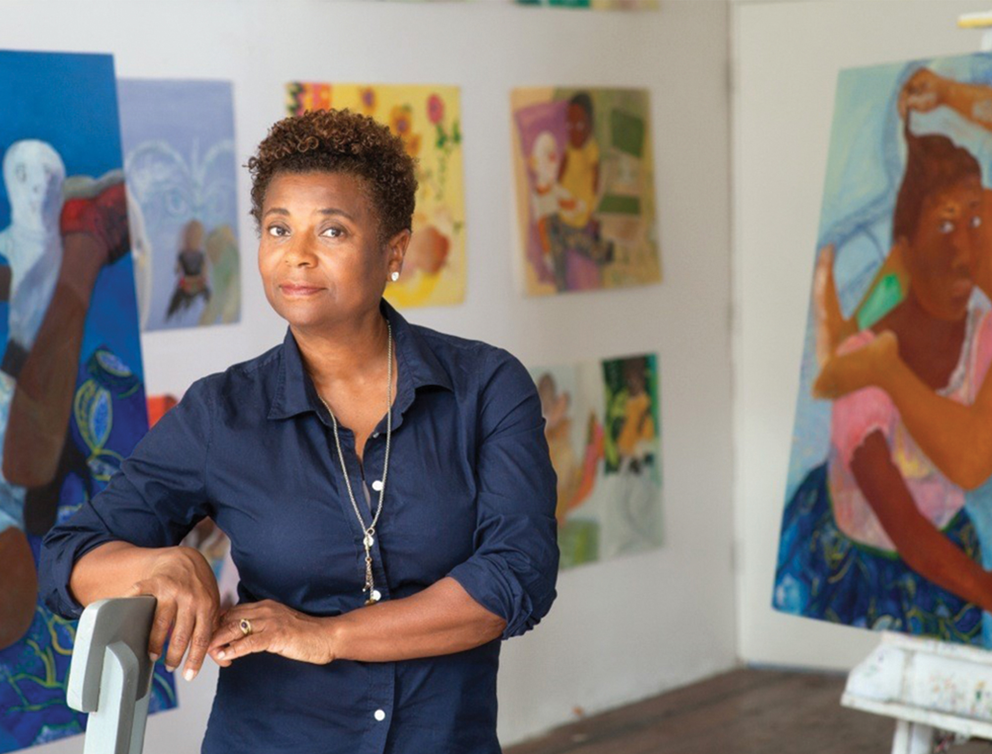 PHILEMONA WILLIAMSON Headshot of her in her studio with paintings by her in the background