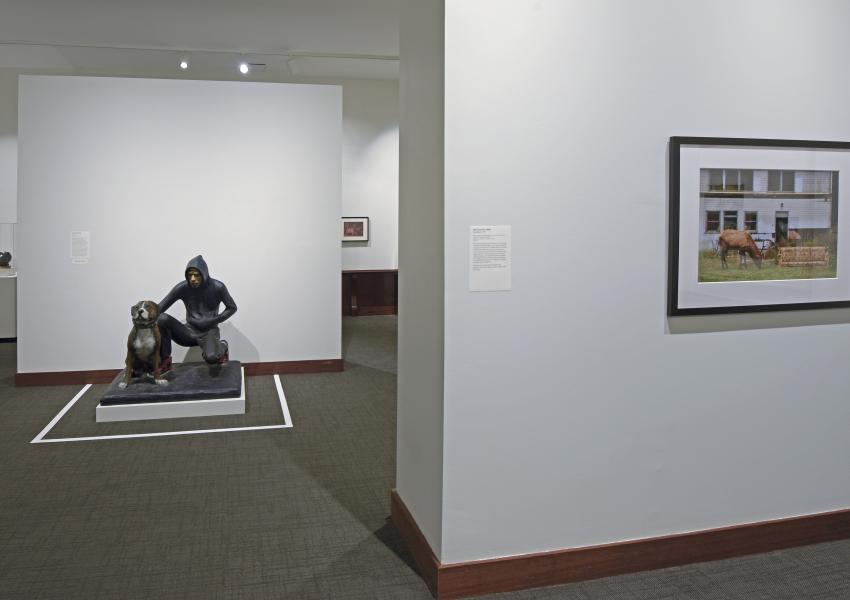 Gallery view in the uncaged exhibition. A painting and a sculpture of a teen and dog are in view.