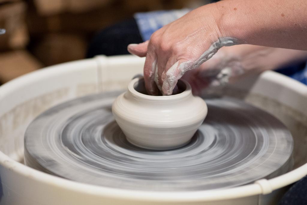 A student's hands are shaping a pot on the pottery wheel. Only their hands are visible. 