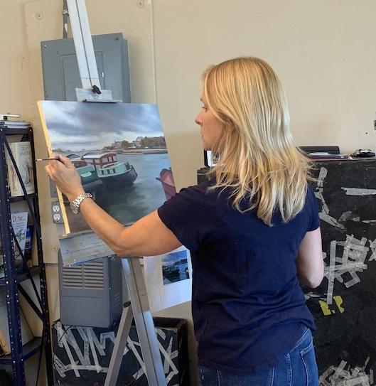 A student is facing away from the camera, working on their oil painting of boats in a canal in venice.