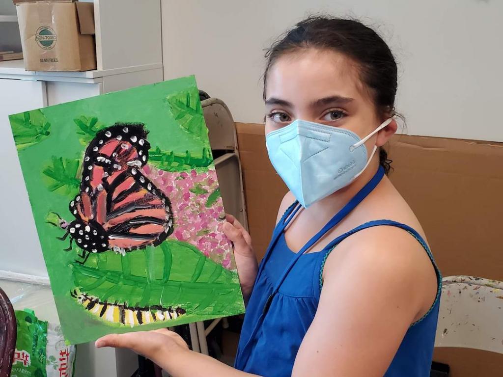 A young student showing off their painting of a butterfly at camp.