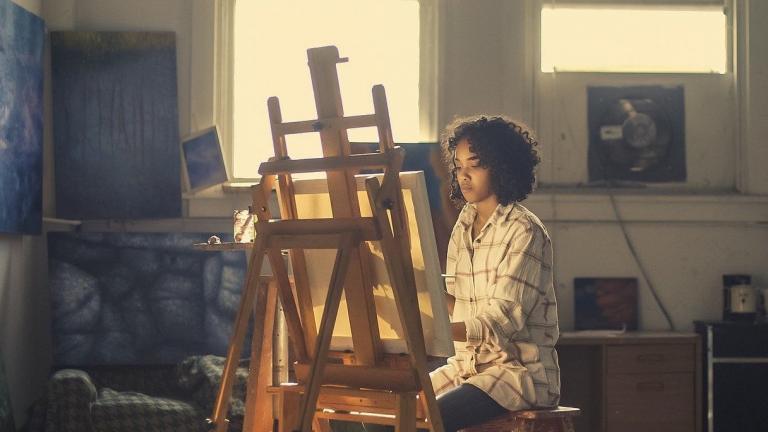 I'm an image! a woman is painting on an easel in a home studio/ She is focused on her art and is not looking at the camera.