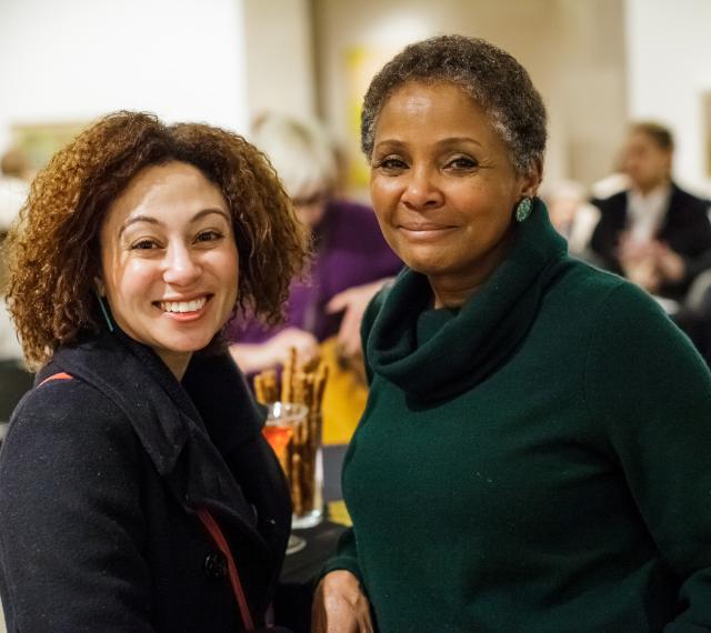 two women leaning on a high top table and smiling during free first thursday