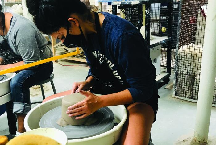 A teen is working on a pottery wheel.
