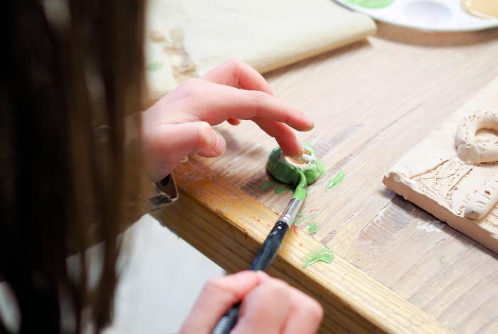 A child's hand painting glaze onto a clay piece