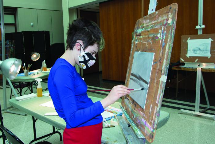 a teen student is painting on an easel. She is not facing the camera.