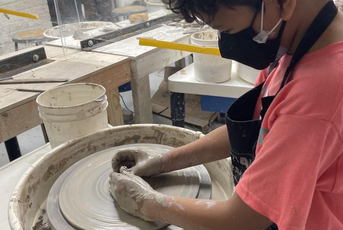 A young student is throwing a pot on the wheel.