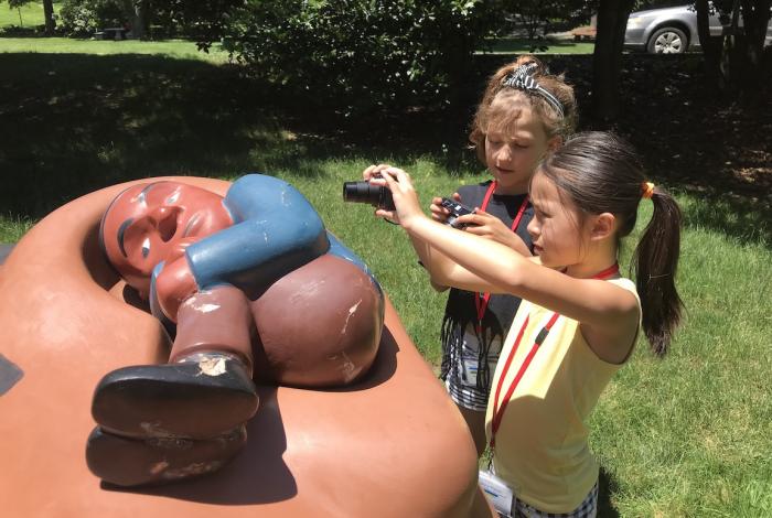 Two young students taking a picture of a sculpture outside on museum grounds.