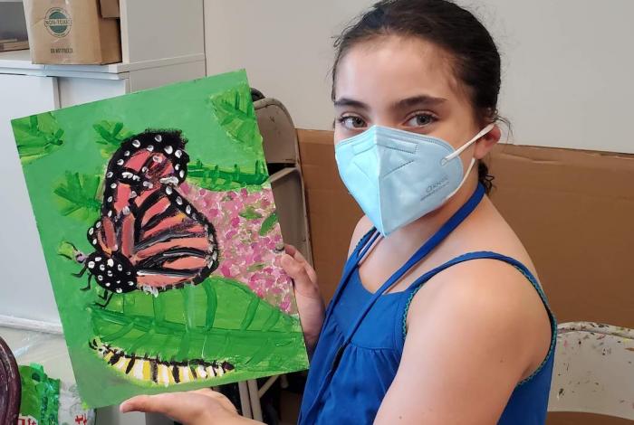 A young student showing off their painting of a butterfly at camp.