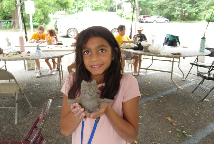 Camper holding up their clay figurine they crafted in SummerART Camp (Ceramic Hand-building)